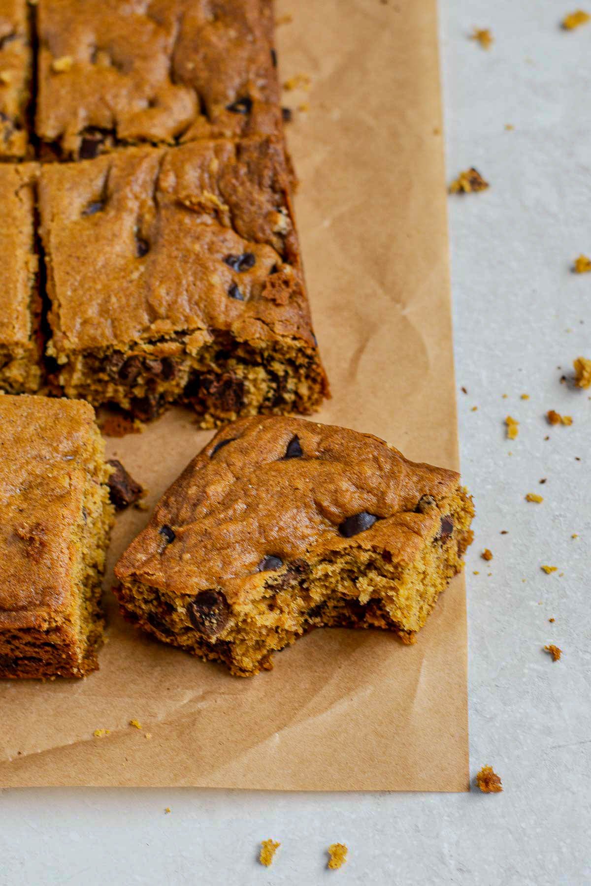 Close-up of soft, chewy pumpkin chocolate chip cookie bars with a bite taken out, showing gooey chocolate chips and moist texture