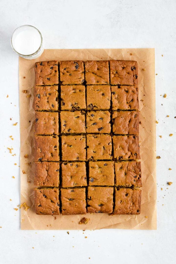 Pumpkin chocolate chip cookie bars cut into squares on parchment paper, ready to serve with a glass of milk.