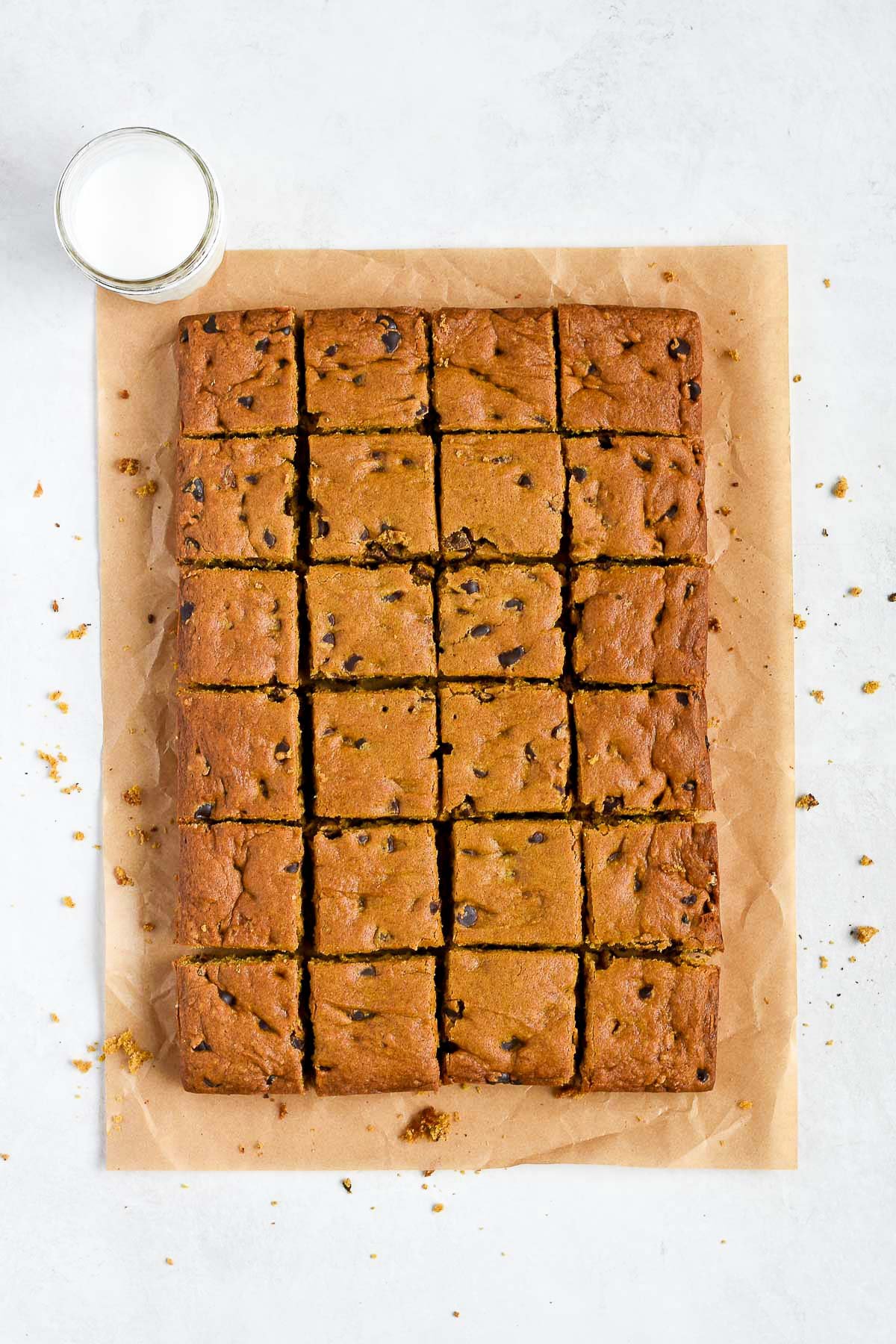 Pumpkin chocolate chip cookie bars cut into squares on parchment paper, ready to serve with a glass of milk.