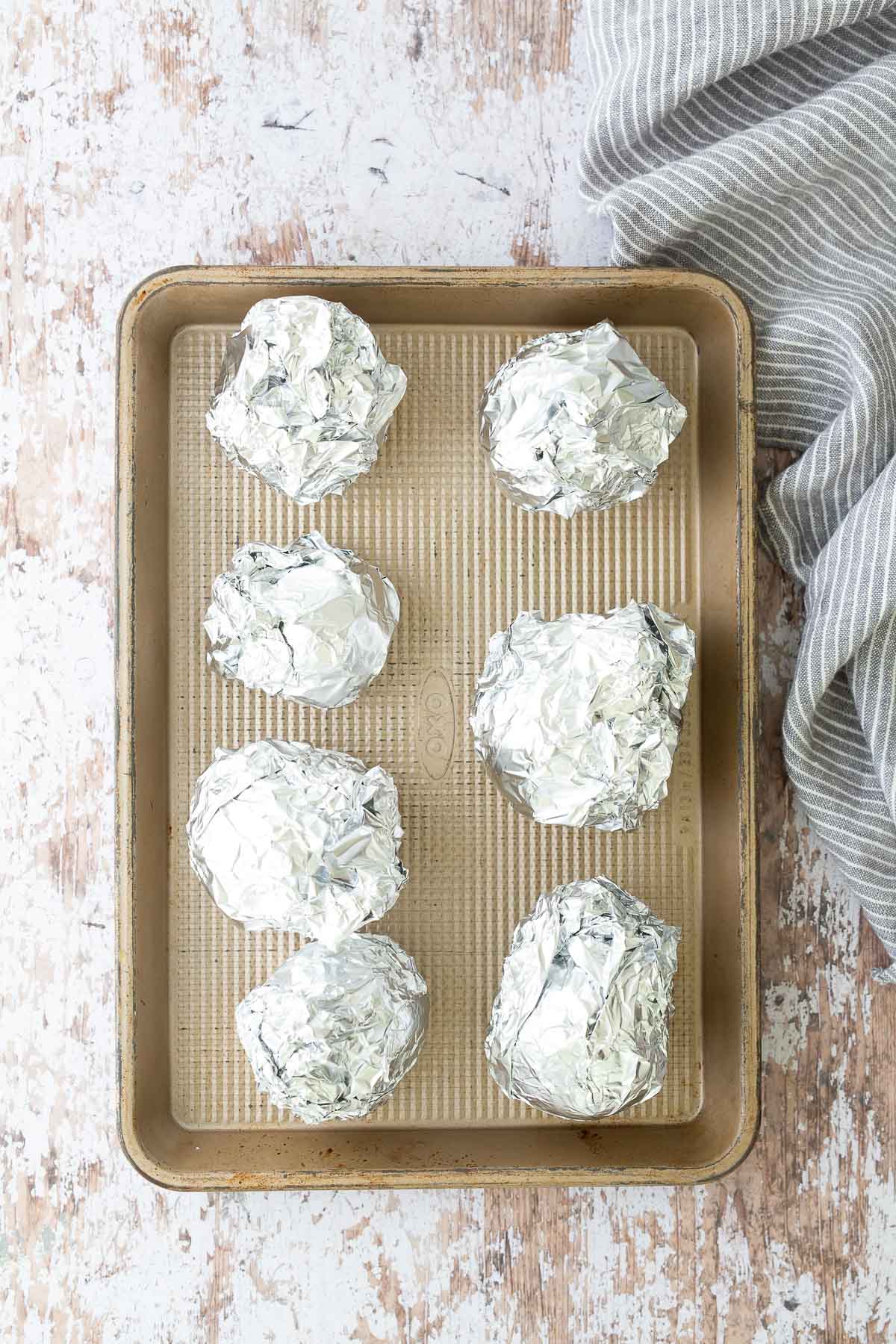 Beets wrapped in aluminum foil on a baking sheet before roasting to make roasted beet salad.