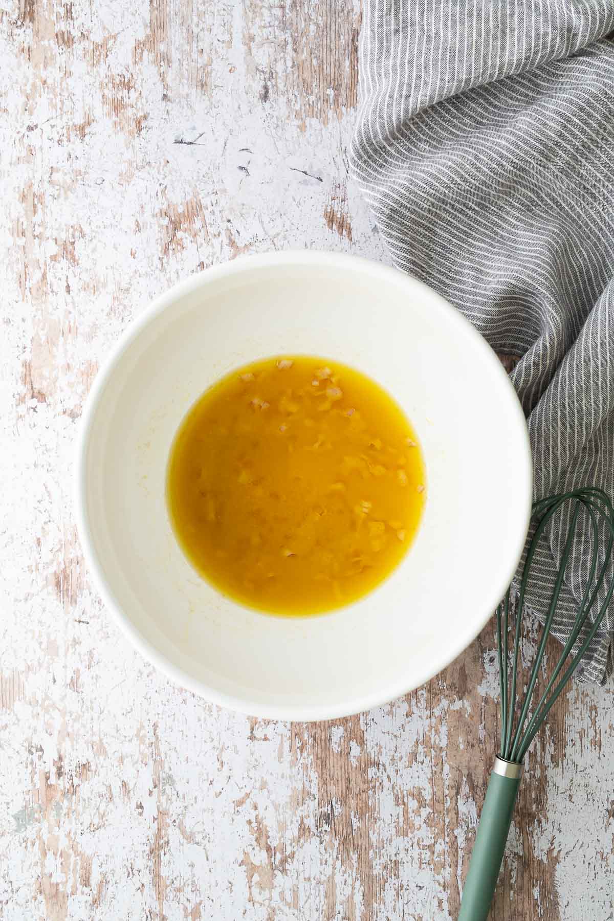 Homemade Dijon and red wine vinaigrette in a white bowl with whisk and striped cloth in background.