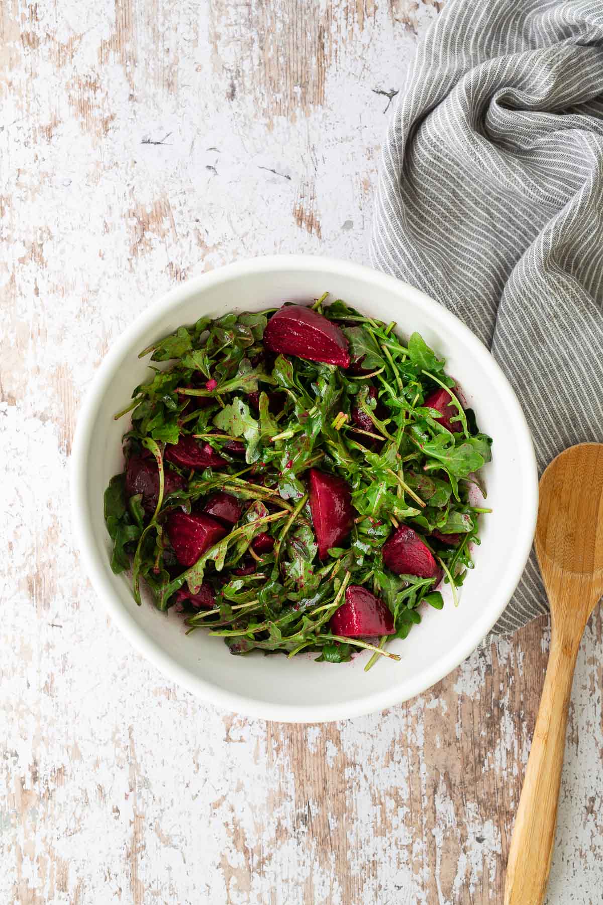 Bowl of roasted beet salad tossed with arugula and vinaigrette before adding feta and pistachios.