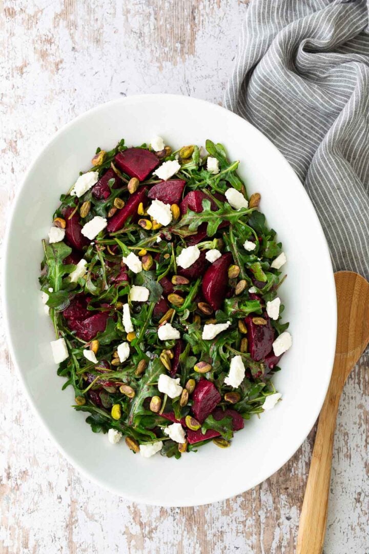 Roasted beet salad with arugula, feta cheese, and pistachios in a large white serving bowl.