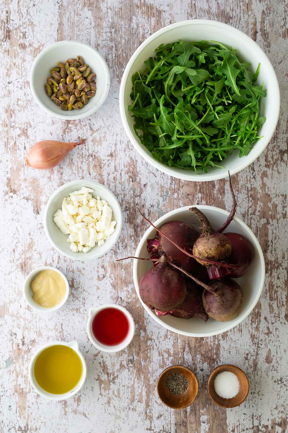 Flat lay of roasted beet salad ingredients including beets, arugula, feta, pistachios, shallot, Dijon mustard, olive oil, and red wine vinegar.