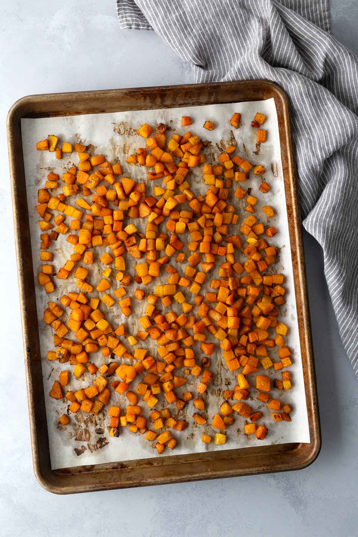 Cubed butternut squash roasted on a parchment-lined baking sheet for fall salad.