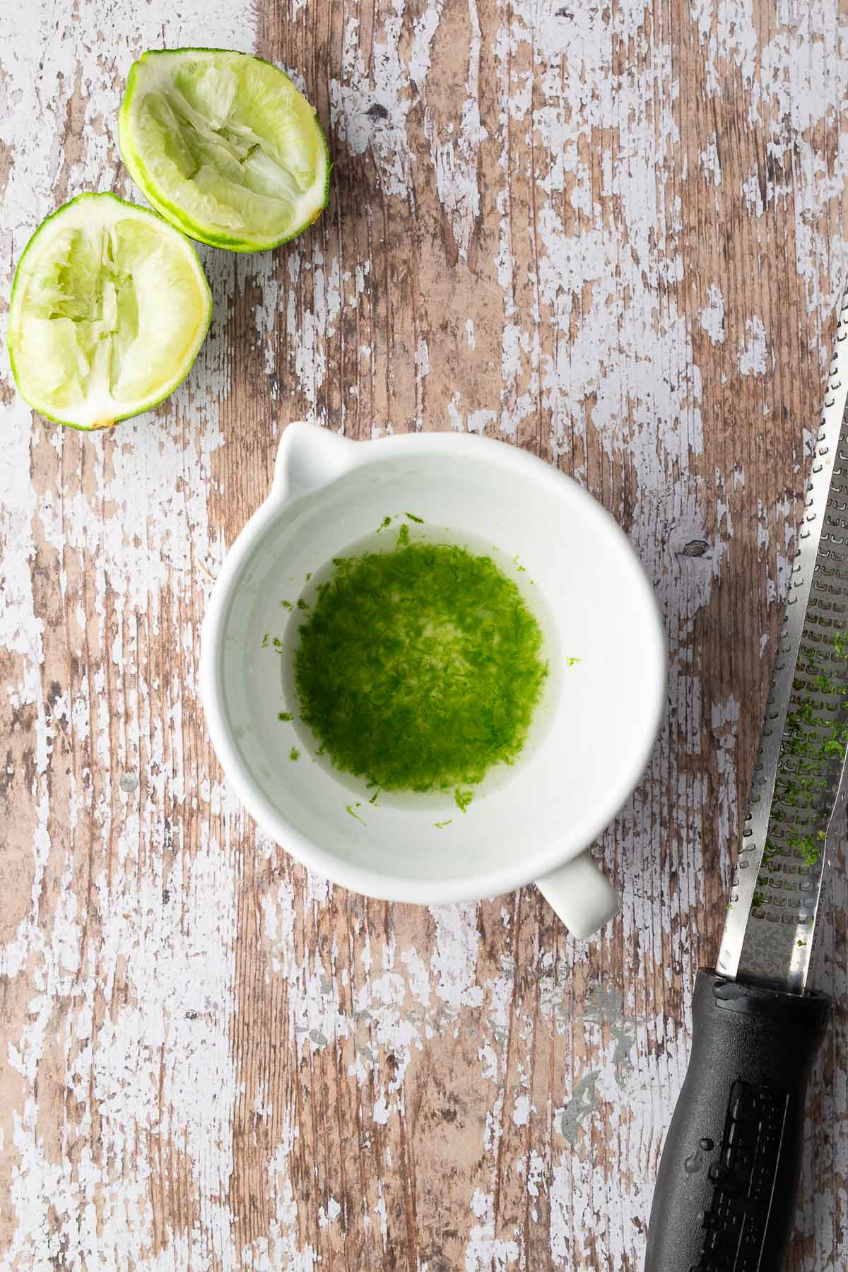 Fresh lime zest and juice in a white bowl on rustic wood surface for tomato corn cucumber avocado salad dressing.