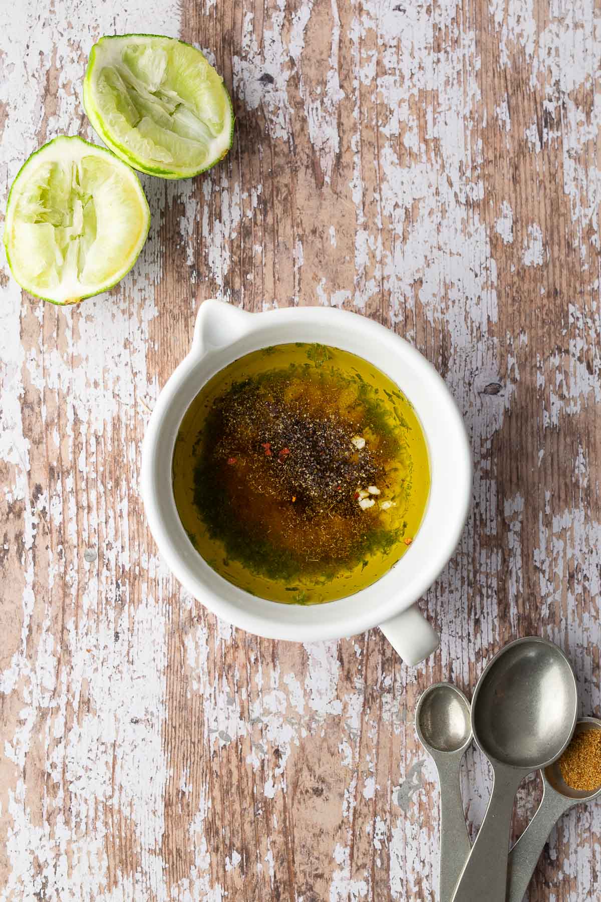 Olive oil, spices, and seasonings mixed with lime juice in a white bowl to make avocado corn cucumber tomato salad dressing.