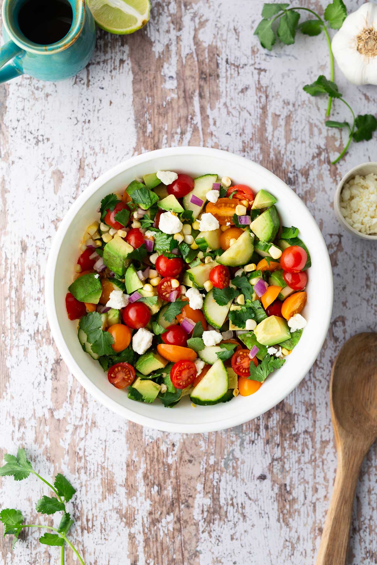 Colorful tomato corn cucumber avocado salad in a white bowl with feta, red onion, and cilantro.